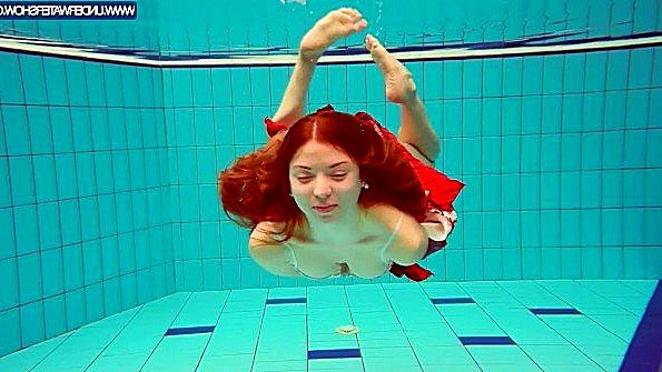 Рыжая барышня плавает под водой и раздевается